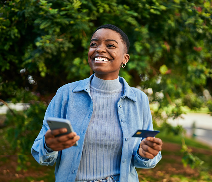 woman outdoors smiling with her phone and debit card